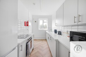 A modern kitchen with white cabinetry, a herringbone wood floor, a window, and a view of trees outside. - 4BR House | Near Sizewell (Peasenhall)