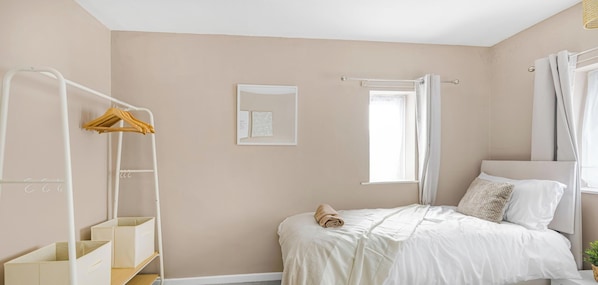A bedroom with a bed, a white wardrobe, a window with curtains, and a small picture on the wall.