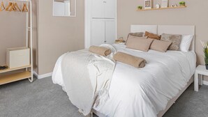 A bedroom with a bed, a wardrobe, a mirror, and a shelf with decorative items. - 4BR House | Near Sizewell (Peasenhall)
