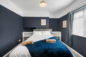 A modern bedroom with a large bed, dark walls, a white headboard, and a bedside table. - 4BR House | Near Sizewell (Peasenhall)