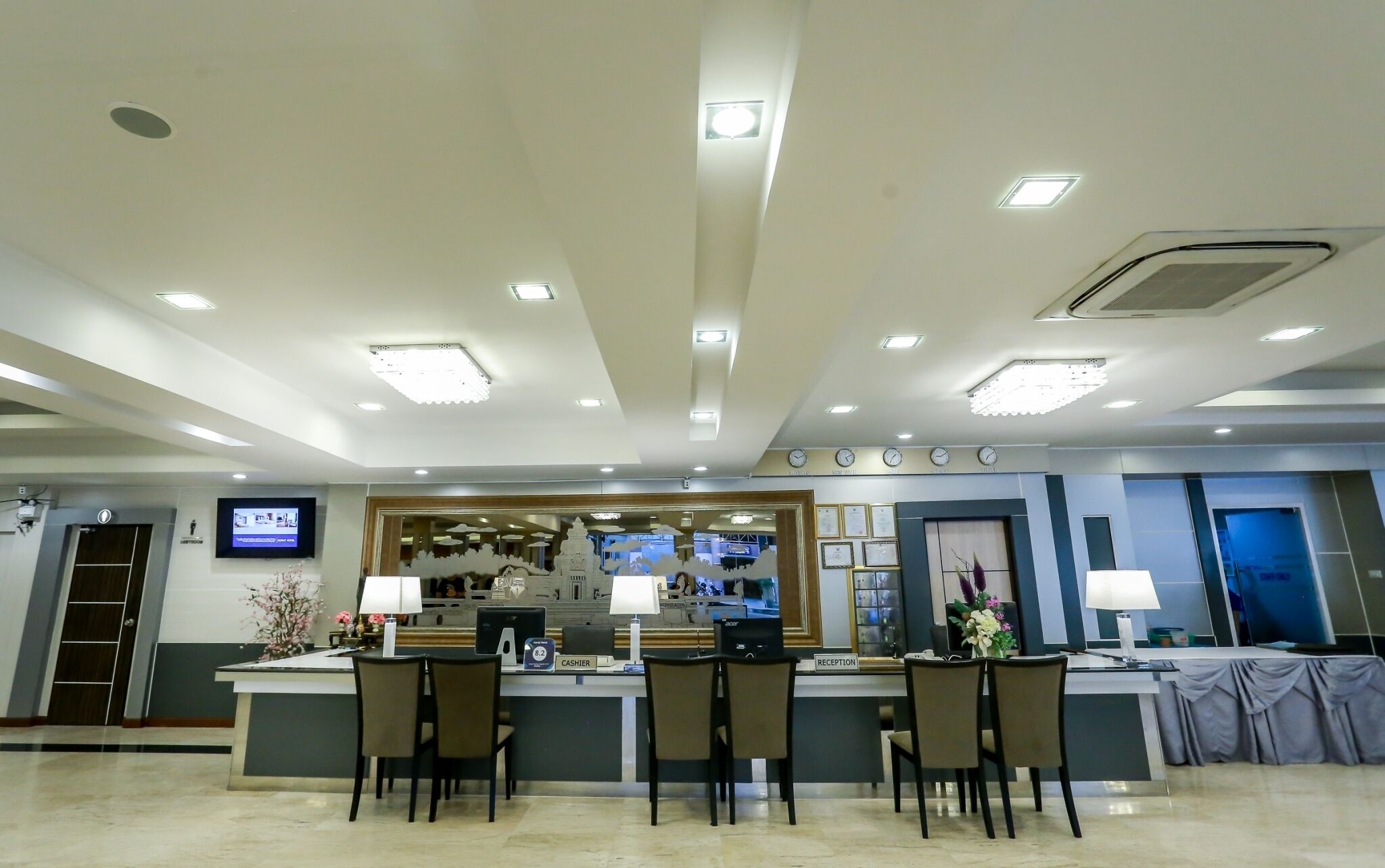 A hotel reception area with a counter, chairs, a clock, and a television screen.