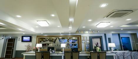 A hotel reception area with a counter, chairs, a clock, and a television screen.