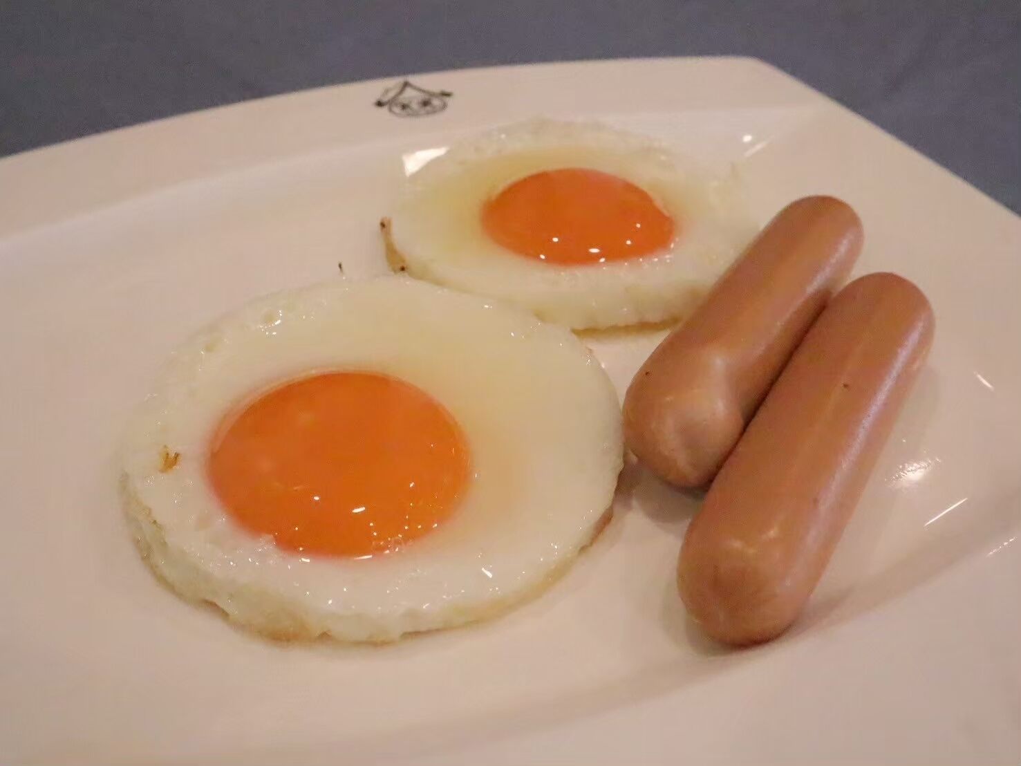 Two sunny-side-up eggs and two sausages on a white plate.