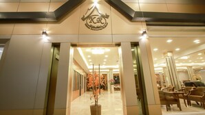 Entrada de hotel com design moderno, exibindo um logotipo em destaque acima da porta, uma área de recepção com balcão e um espaço de estar com cadeiras e mesas.