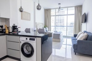 Un appartement moderne comprenant une cuisine, un coin repas, un salon et une grande fenêtre donnant sur la ville.