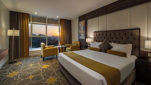 Hotelkamer met een groot bed, twee fauteuils, een klein tafeltje en uitzicht op de ondergaande zon.