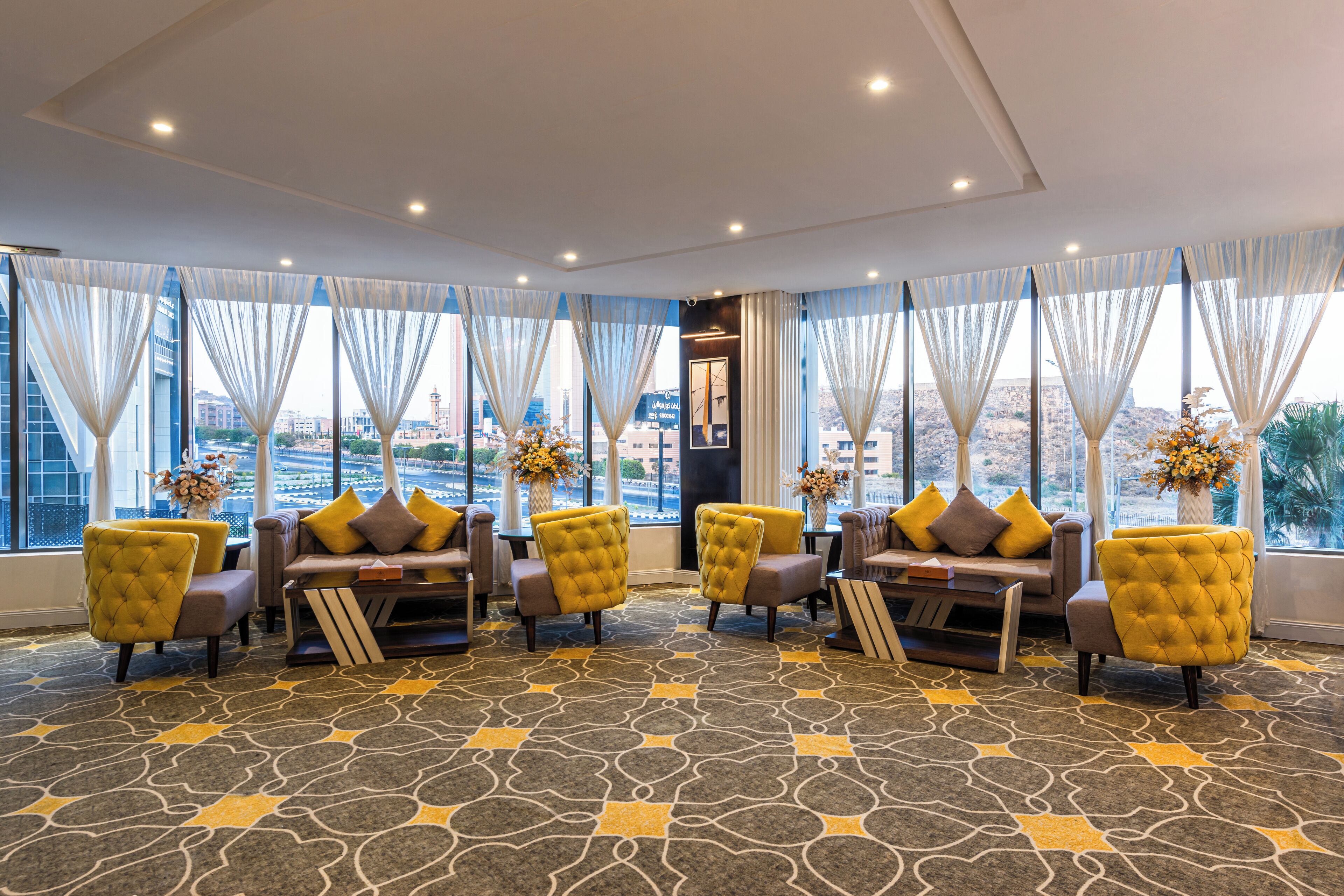 A hotel lobby with a seating area, large windows, and a patterned carpet.