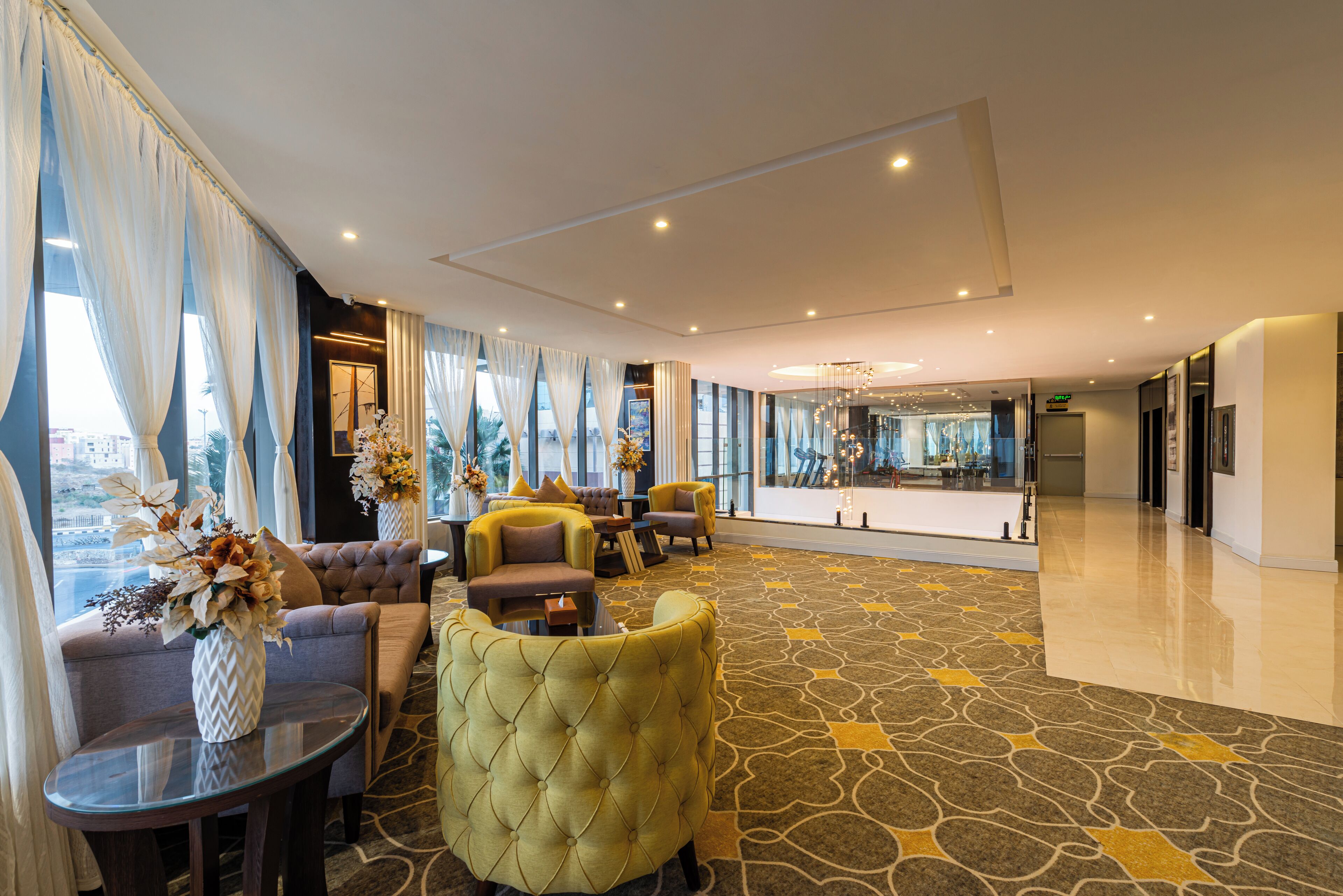 Un moderno vestíbulo de hotel con área de descanso, ventanas amplias y alfombra estampada.