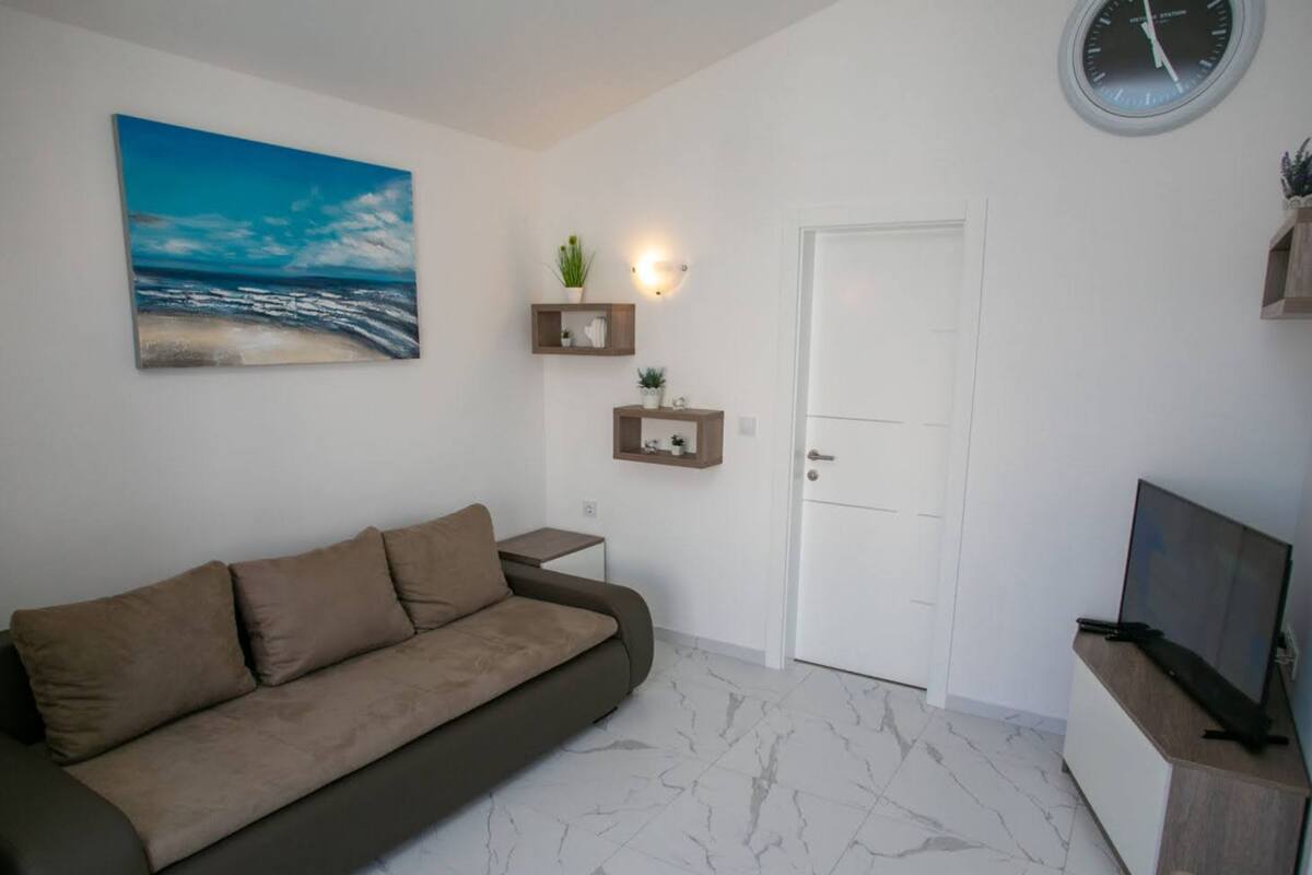 A living room with a sofa, a painting of a beach, a clock, and a door.
