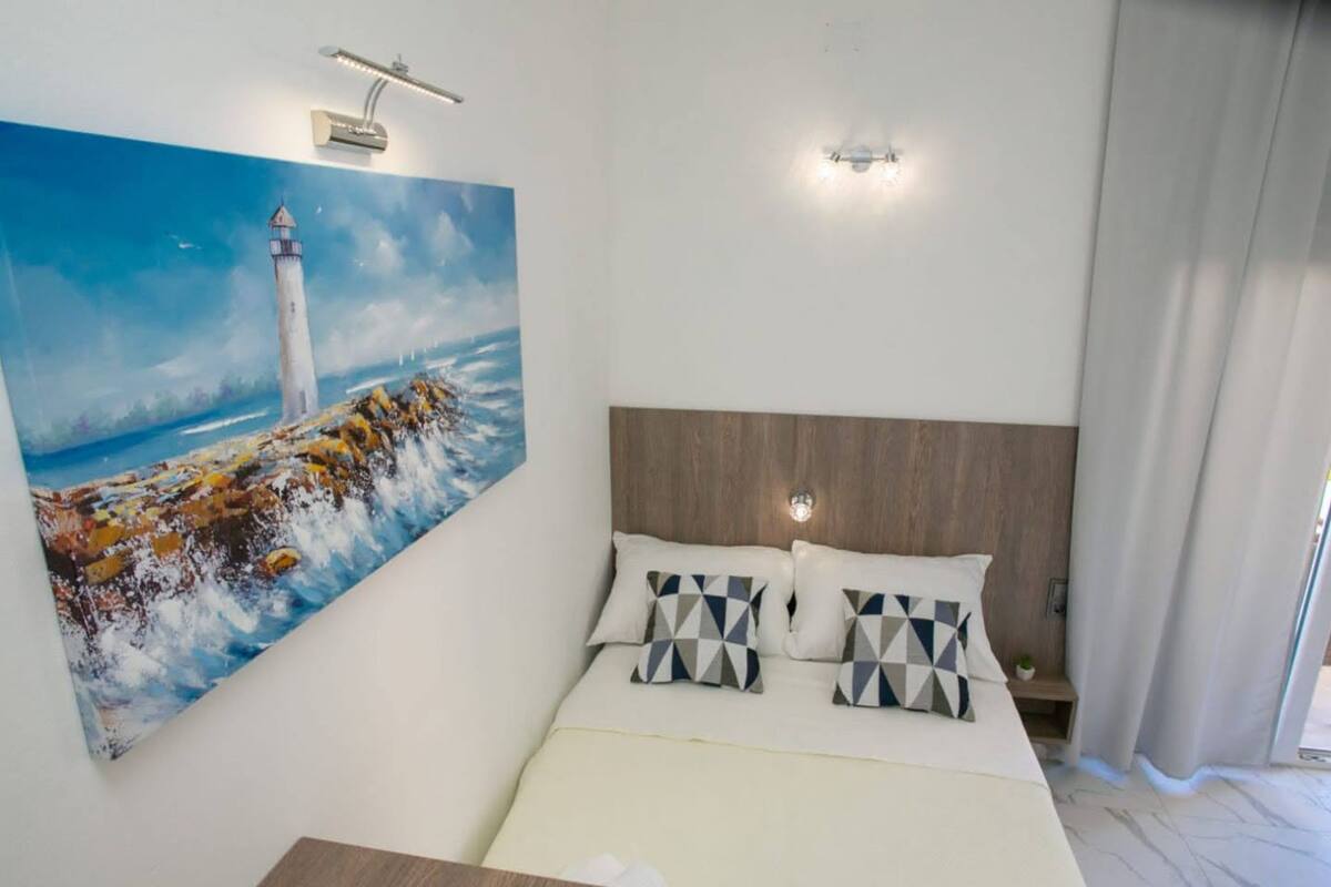 A bedroom with a large painting of a lighthouse, a wooden headboard, and a bedside table.