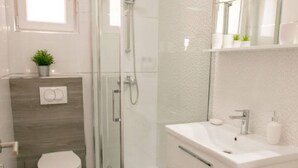 A modern bathroom with a glass shower enclosure, a toilet, a sink with a mirror, and a small potted plant on the wall. - Apartments Sun Dance 2 With Heated Pool (Novalja)