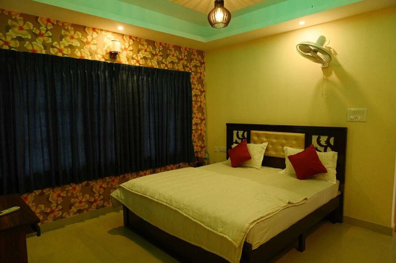 A bedroom with a bed, a nightstand, a wall-mounted fan, and a floral-patterned curtain.