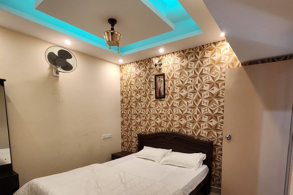A bedroom with a bed, a ceiling fan, and a geometric-patterned wall.