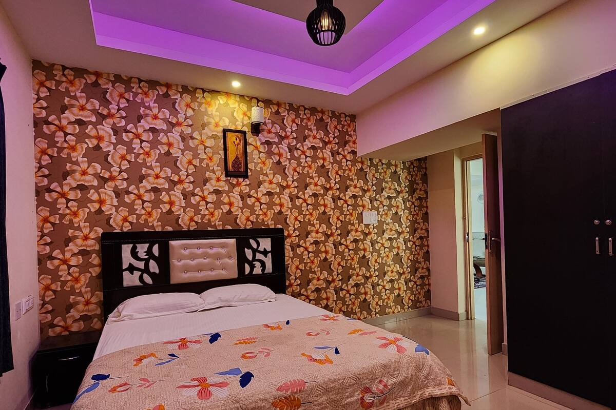 A modern bedroom with a floral-patterned wall, a bed with a patterned bedspread, and a ceiling light fixture.