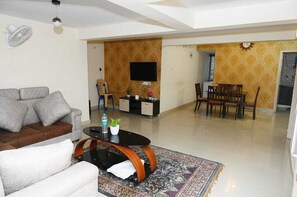 A living room with a sofa, a coffee table, a TV, and a dining area with chairs and a table. - Aadams Suites (Bengaluru)