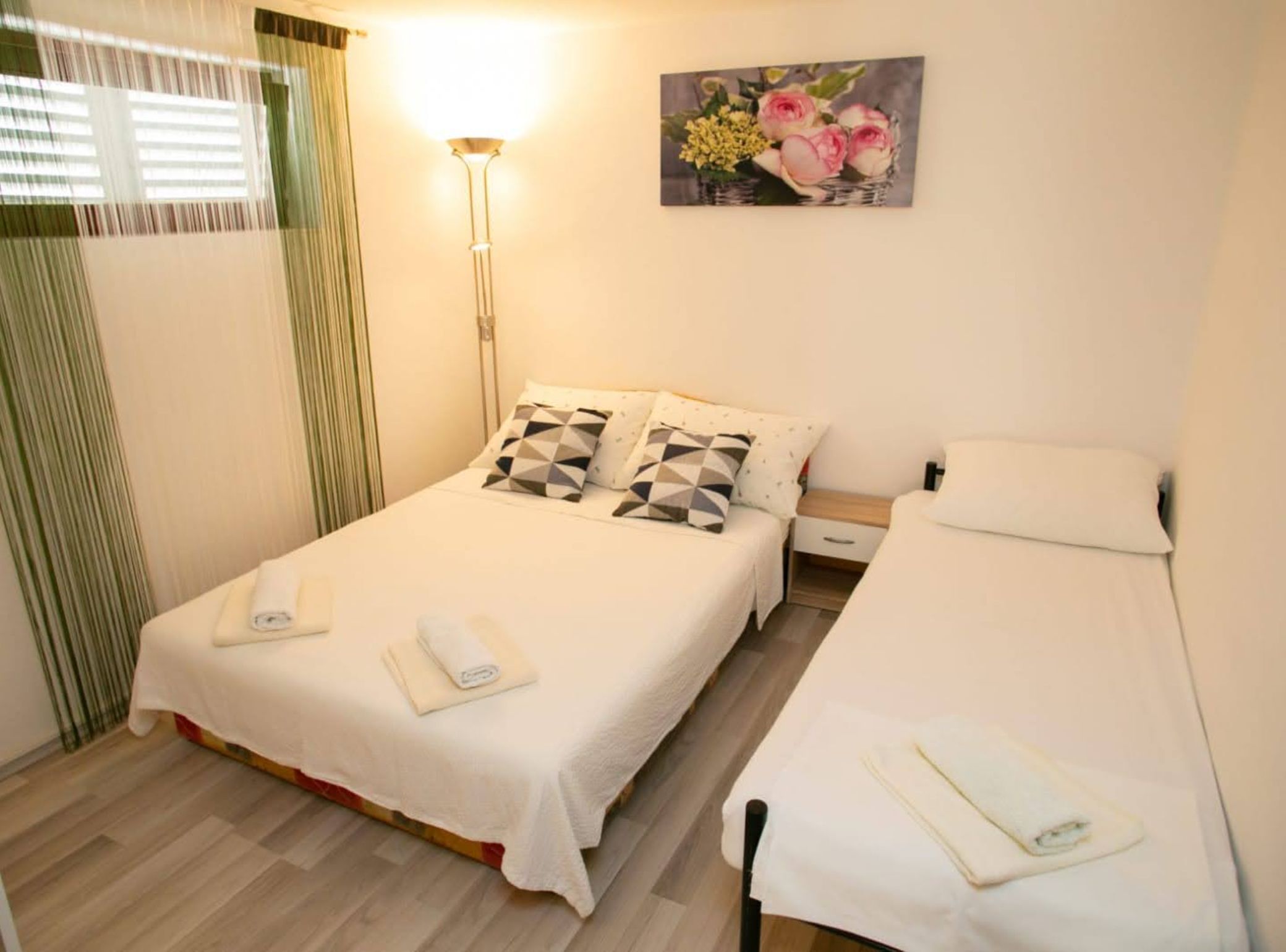 Une chambre d’hôtel avec deux lits, une table de chevet, une lampe et un tableau représentant des fleurs accroché au mur.