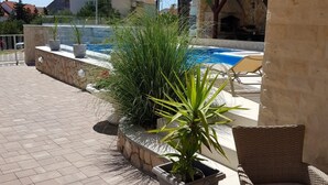 A pool area with a stone wall, potted plants, and outdoor furniture. - Apartments Sun Dance With Heated Pool (Novalja)