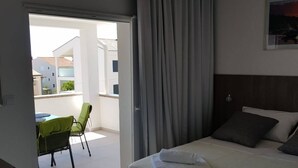 A hotel room with a bed, a chair, and a view of the outside. - Apartments Sun Dance With Heated Pool (Novalja)