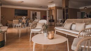 A spacious living area with a round table, wicker furniture, and a large flat-screen TV mounted on the wall. - Hotel MioMio (Tignale)