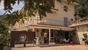 A hotel with a stone facade, outdoor seating, and a sign reading "MIO MIO HOTEL". - Hotel MioMio (Tignale)