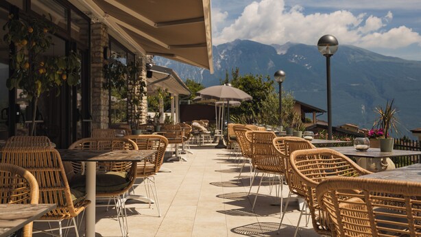 An outdoor cafe with wicker furniture and a view of mountains. - Hotel MioMio (Tignale)