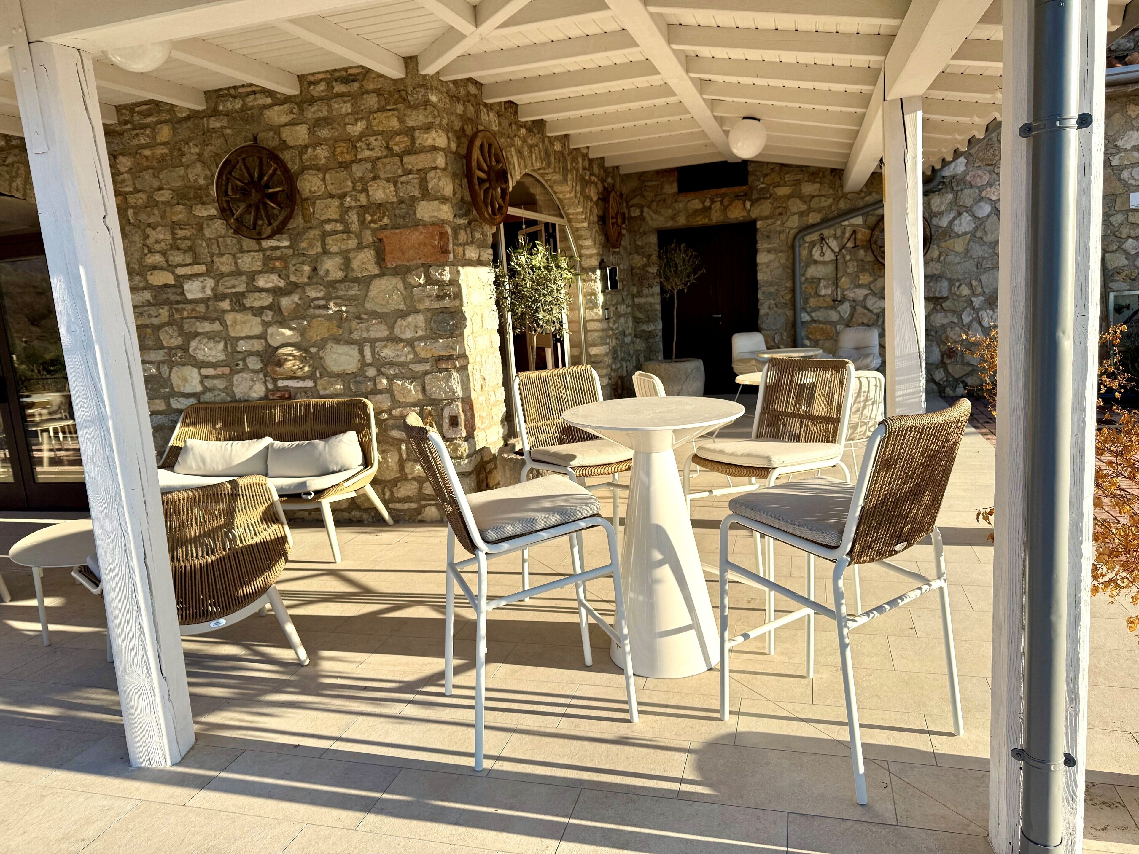 An outdoor patio with stone walls, wicker furniture, and a white ceiling.