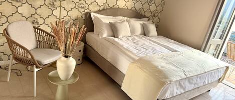 A bedroom with a bed, a chair, a vase with dried plants, and a floor lamp.