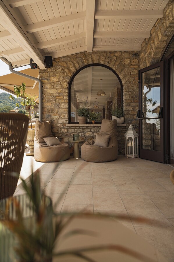 A covered patio with stone walls, two beige bean bag chairs, a white lantern, and a large arched mirror.