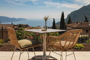 A terrace with wicker chairs and a table, overlooking a scenic view of mountains and a body of water. - Hotel MioMio (Tignale)