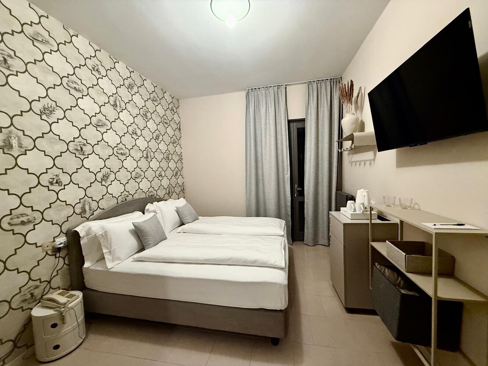 A modern hotel room with a bed, a desk, a television, and a patterned wall.