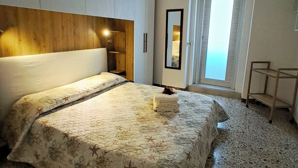 A bedroom with a bed, a wooden headboard, a hanging light fixture, a mirror, and a door leading to a balcony.