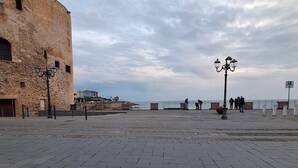 A paved square with a historic building on one side and a waterfront view.