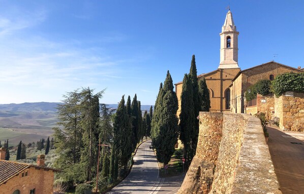 Une église historique dotée d’un clocher, entourée de murs de pierre et de grands cyprès.