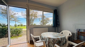 Quarto com mesa e cadeiras, vista para área verde e um corpo d'água através de amplas janelas, e piso de azulejos.