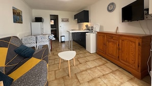 Espaço compacto com sofá, mesa de jantar, cozinha e televisão fixada na parede.