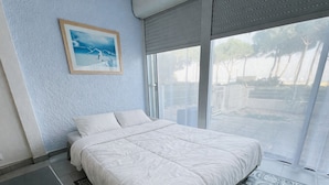 Ein Schlafzimmer mit einem großen Bett, einem kleinen Tisch, einem gemusterten Teppich und einem Fenster mit Blick auf Bäume und einen Zaun.