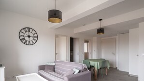 A modern living room with a sofa, a small table, and a dining table with chairs. There are two pendant lights hanging from the ceiling.