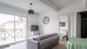 A modern living room with a sofa, a television on a stand, a wall clock, and a dining area with a table and chairs.