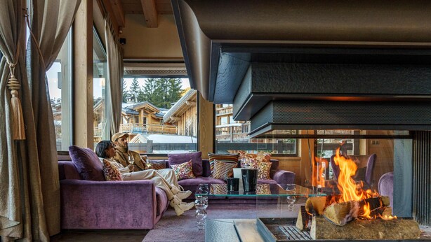 A cozy living room with a fireplace, purple sofas, and a glass coffee table.
