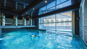 An indoor swimming pool with clear water, large windows, and a view of a historic building.