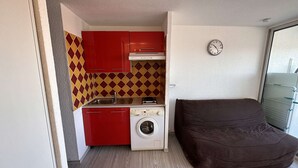 A compact kitchen with red cabinets, a washing machine, and a brown sofa.