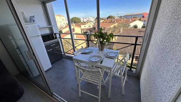 A balcony with a dining table set for four, overlooking a cityscape.