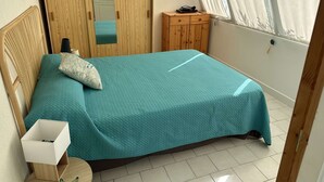 A bedroom with a bed, a wardrobe, a small table, and a window with curtains. - 3-room apartment, private terrace, sleeps 6 in Port Camargue (Port Camargue)