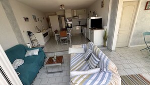 A living room with a sofa and armchair, a dining table with chairs, a kitchen area with appliances, and a TV. - 3-room apartment, private terrace, sleeps 6 in Port Camargue (Port Camargue)