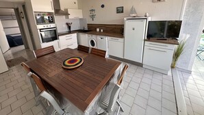 A modern kitchen with white cabinets, a wooden dining table, and a built-in washing machine. - 3-room apartment, private terrace, sleeps 6 in Port Camargue (Port Camargue)