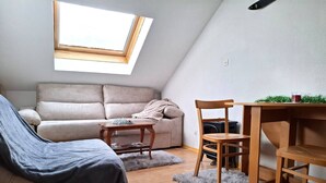 A cozy loft apartment with a sloped ceiling, a sofa, a chair, a small wooden table, and a radiator.