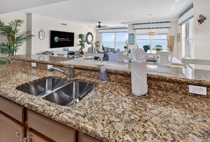 A kitchen with granite countertops, stainless steel sink, and a ceiling fan.