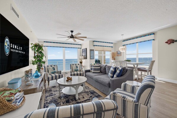A spacious living room with a large window, a ceiling fan, and a view of the ocean.