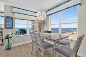 A dining area with a view of the beach, a decorative wall sign, and a modern light fixture.