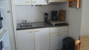 A compact kitchen with white cabinets, a sink, a Bosch coffee maker, and a wooden chair.